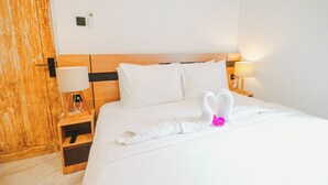 A hotel room with a wooden headboard, white bedding, a lamp on the nightstand, and a swan-shaped towel on the bed. - Queenara Local House (Carangsari)