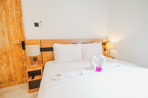 A hotel room with a wooden headboard, white bedding, a lamp on the nightstand, and a swan-shaped towel on the bed. - Queenara Local House (Carangsari)