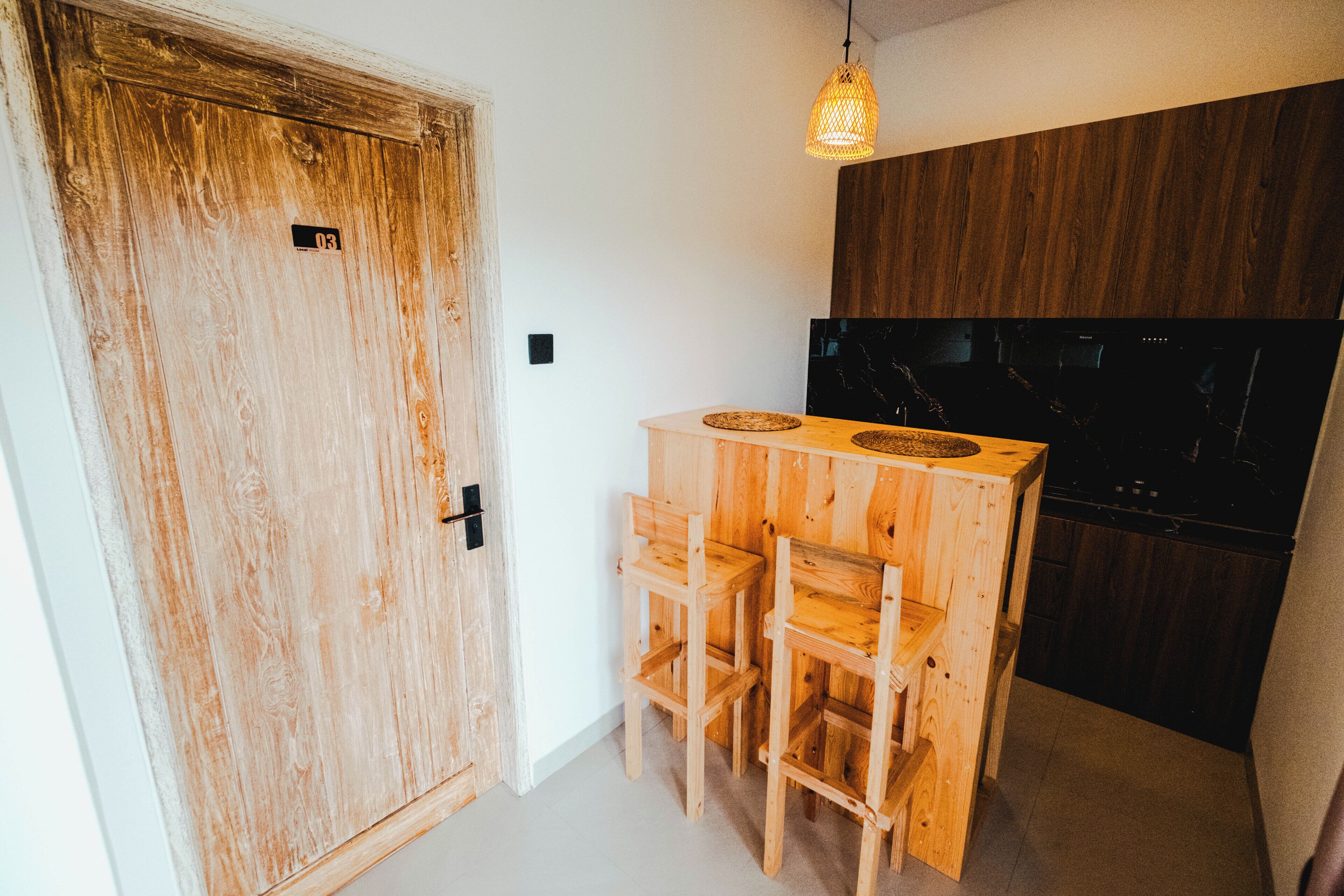 A wooden door with a number plate, a small wooden table with chairs, a hanging light fixture, and a dark-colored cabinet.