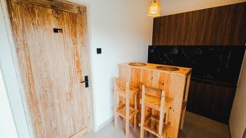 A wooden door with a number plate, a small wooden table with chairs, a hanging light fixture, and a dark-colored cabinet.