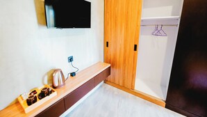 A modern bathroom with a wooden vanity, a flat-screen TV mounted on the wall, and a towel rack with a towel hanging. - Queenara Local House (Carangsari)