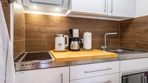 Moderni keittiö, jossa on valkoiset kaapit, puinen välitila, sisäänrakennettu liesi, kahvinkeitin ja pesuallas.
