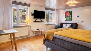 Moderni huone, jossa on sänky, televisio, pieni pöytä ja ikkuna, jossa on verhot.