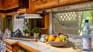 A kitchen area with wooden cabinets, a bowl of fruit, a bottle of water, and a small plant on the counter. - Caravan 'La Pura Vida' with Private Terrace (Brandenburg an der Havel)