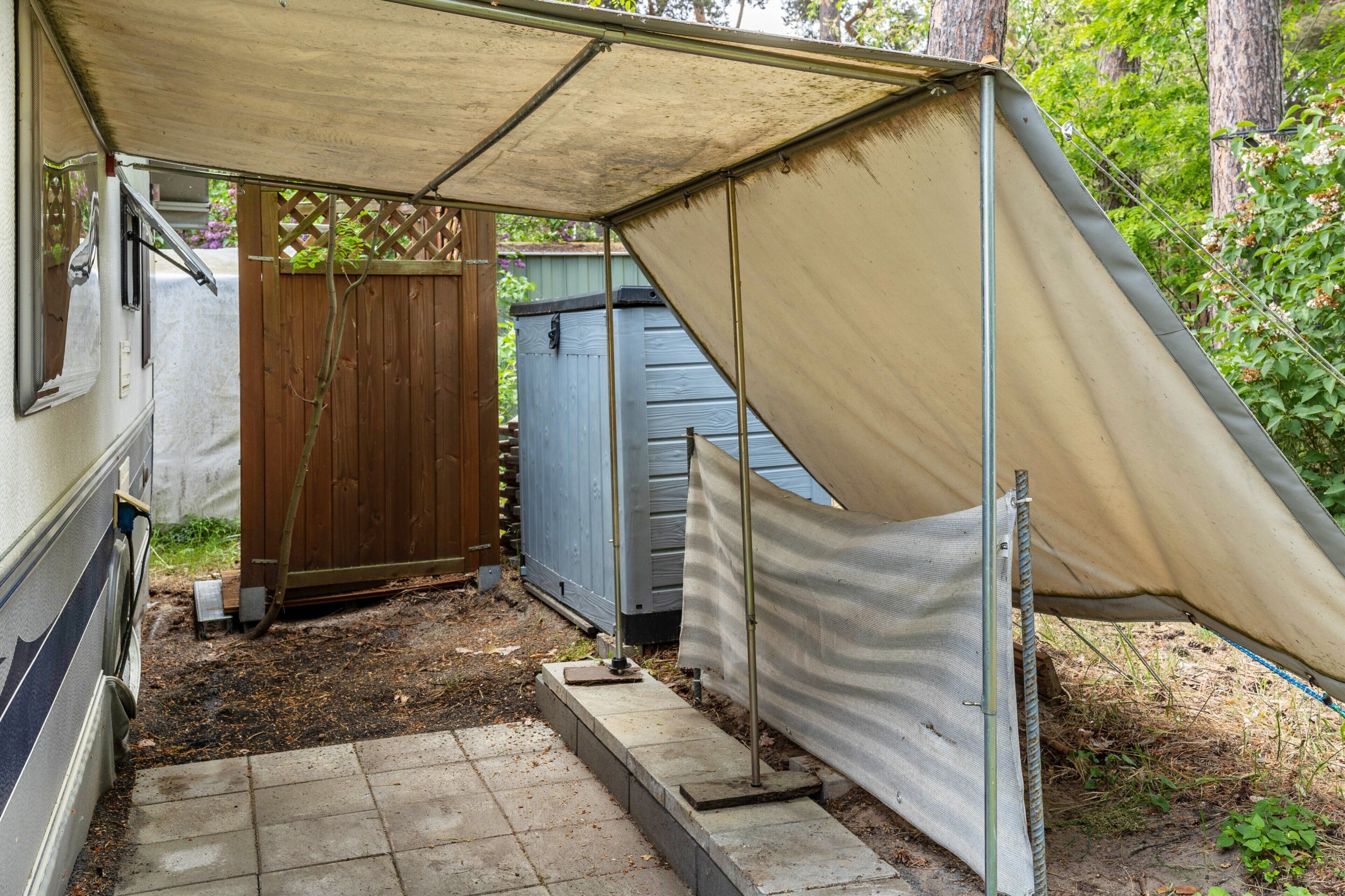 Un espace extérieur abrité, délimité par une clôture en bois, une porte en métal et un chemin en béton menant à un bâtiment.