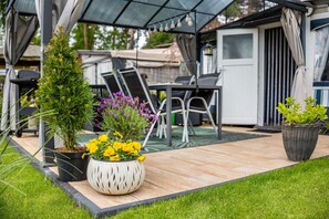 Een terras met buitenmeubilair, plantenpotten en een overdekt zitgedeelte.