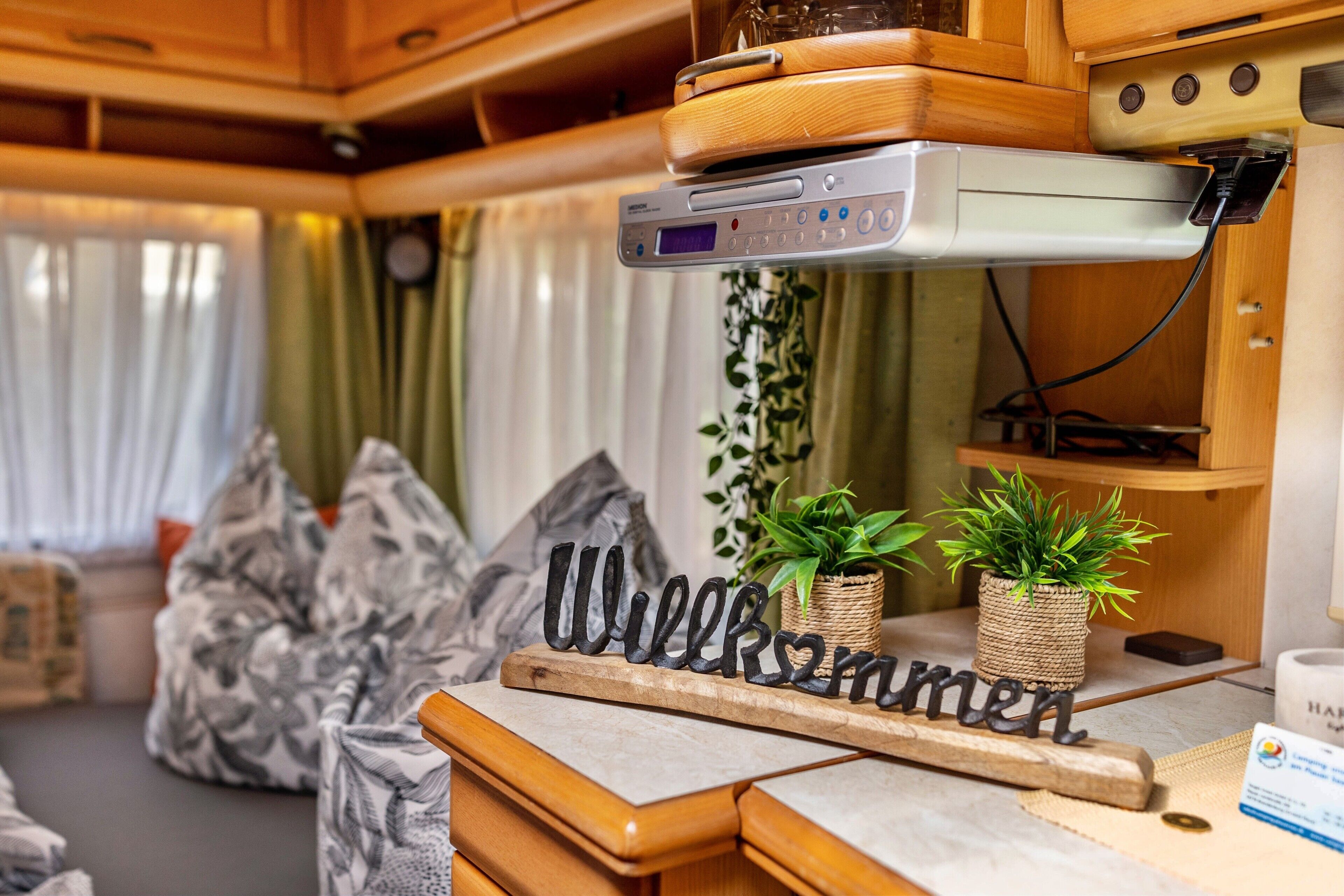 A kitchenette with a coffee maker, a 'Welcome' sign, and two potted plants.