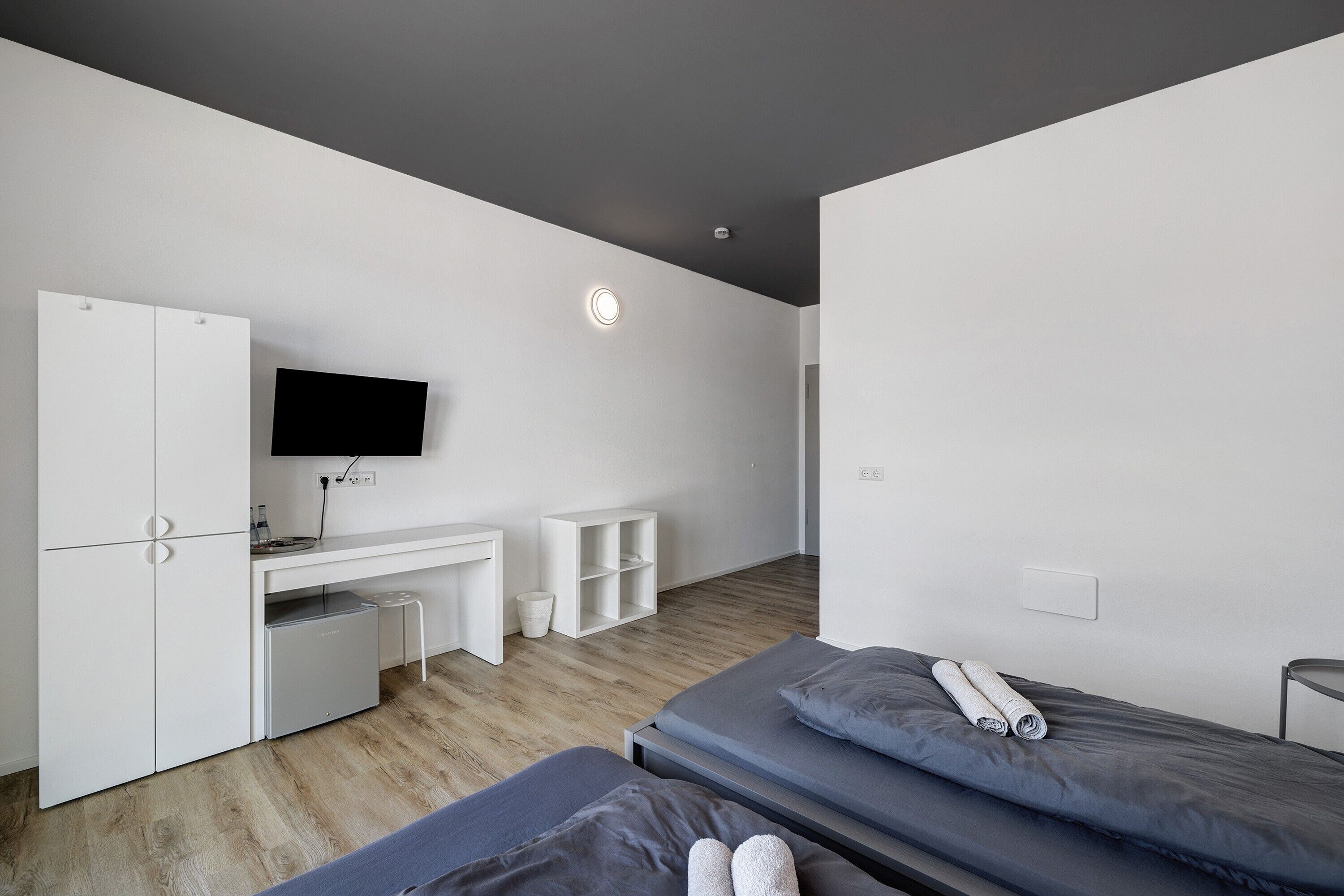 Ein modernes Schlafzimmer mit Bett, Schreibtisch, Fernseher und Kleiderschrank.