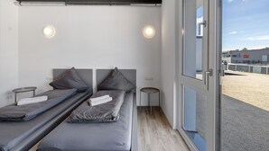 A room with two beds, a small round table, and a large window. - Room '12' with Wi-Fi (Dußlingen)