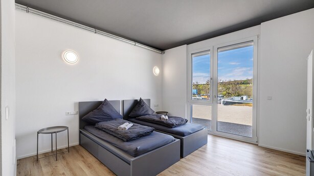 A modern bedroom with two beds, a small table, and a large window with a view. - Room '12' with Wi-Fi (Dußlingen)