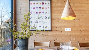 A dining table with a bowl of fruit, a vase with flowers, and a framed botanical illustration on the wall. - Tiny House 'Tanne' in the Heart of the Northern Black Forest (Schömberg)