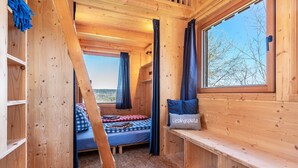 A wooden cabin room with a bed, a bench, and a window overlooking a forest. - Tiny House 'Tanne' in the Heart of the Northern Black Forest (Schömberg)