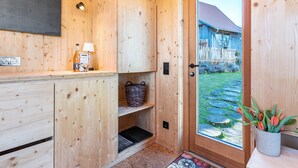 A wooden interior with a door leading to a garden, a shelf with a basket, and a wall-mounted light fixture. - Tiny House 'Tanne' in the Heart of the Northern Black Forest (Schömberg)