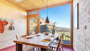 A wooden interior with a dining table set for four, a large window, and a view of the outside.