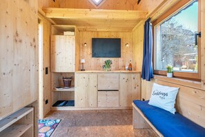 Interior de una cabaña de madera con kitchenette, un banco con cojín y una ventana con cortinas.