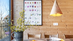 A dining table with a bowl of fruit, a vase with flowers, and a framed botanical illustration on the wall.