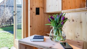 A wooden interior with a glass door, a book titled 'Pistebuch,' and a vase with purple flowers on a wooden table.