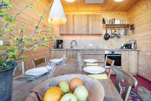 Interior de madera con una mesa de comedor preparada para cuatro personas, un frutero y utensilios de cocina.