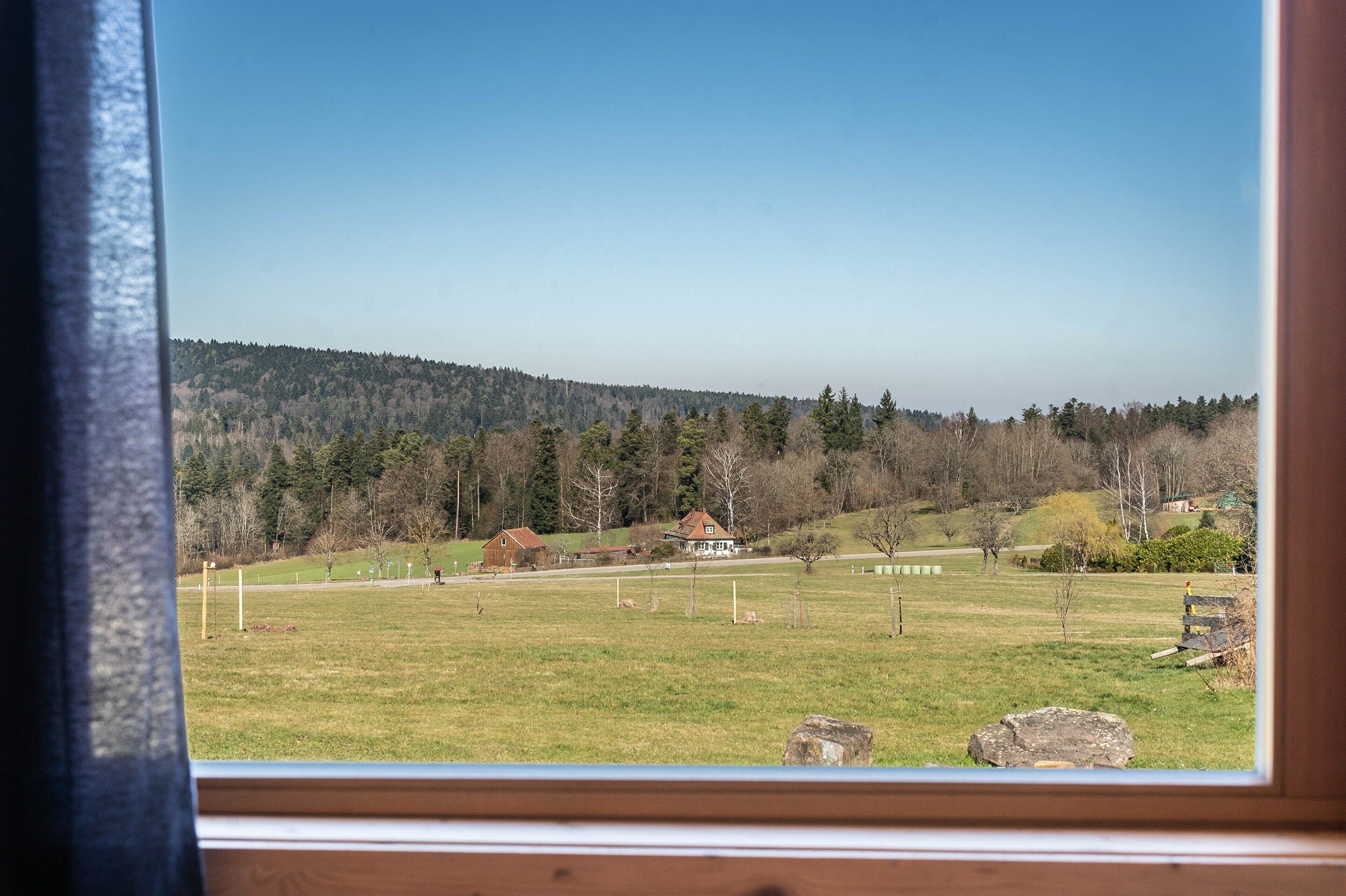 Un paysage rural avec une maison, des champs ouverts et une colline boisée.