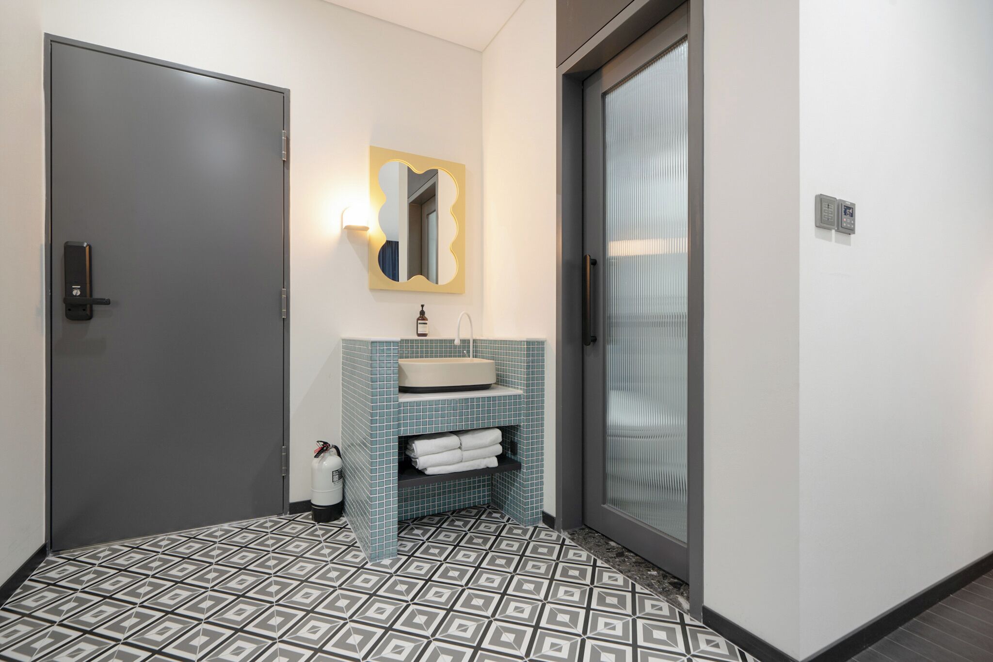 A bathroom with a grey door, a sink with a blue tiled backsplash, and a mirror with a gold frame.