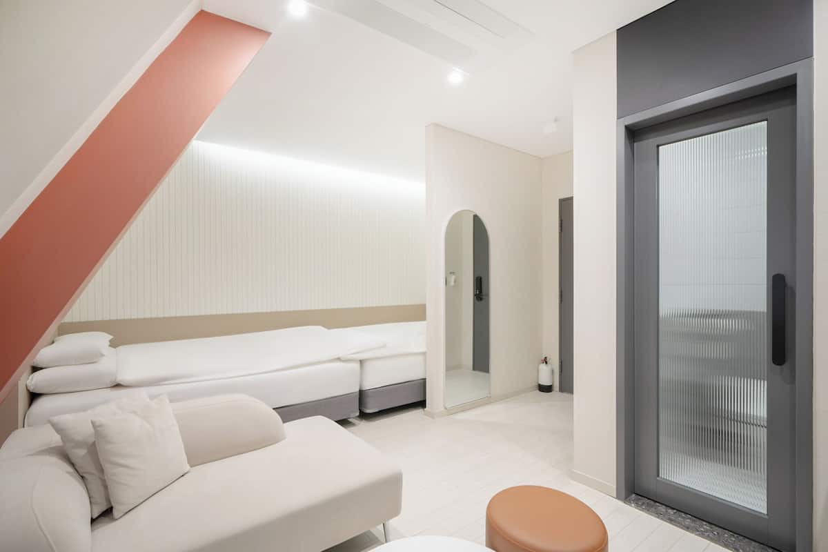 Ett modernt hotellrum med en säng, en soffa, en glasdörr och ett litet badrum.