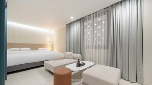 A modern hotel room with a large bed, a sofa, a coffee table, and a small ottoman.