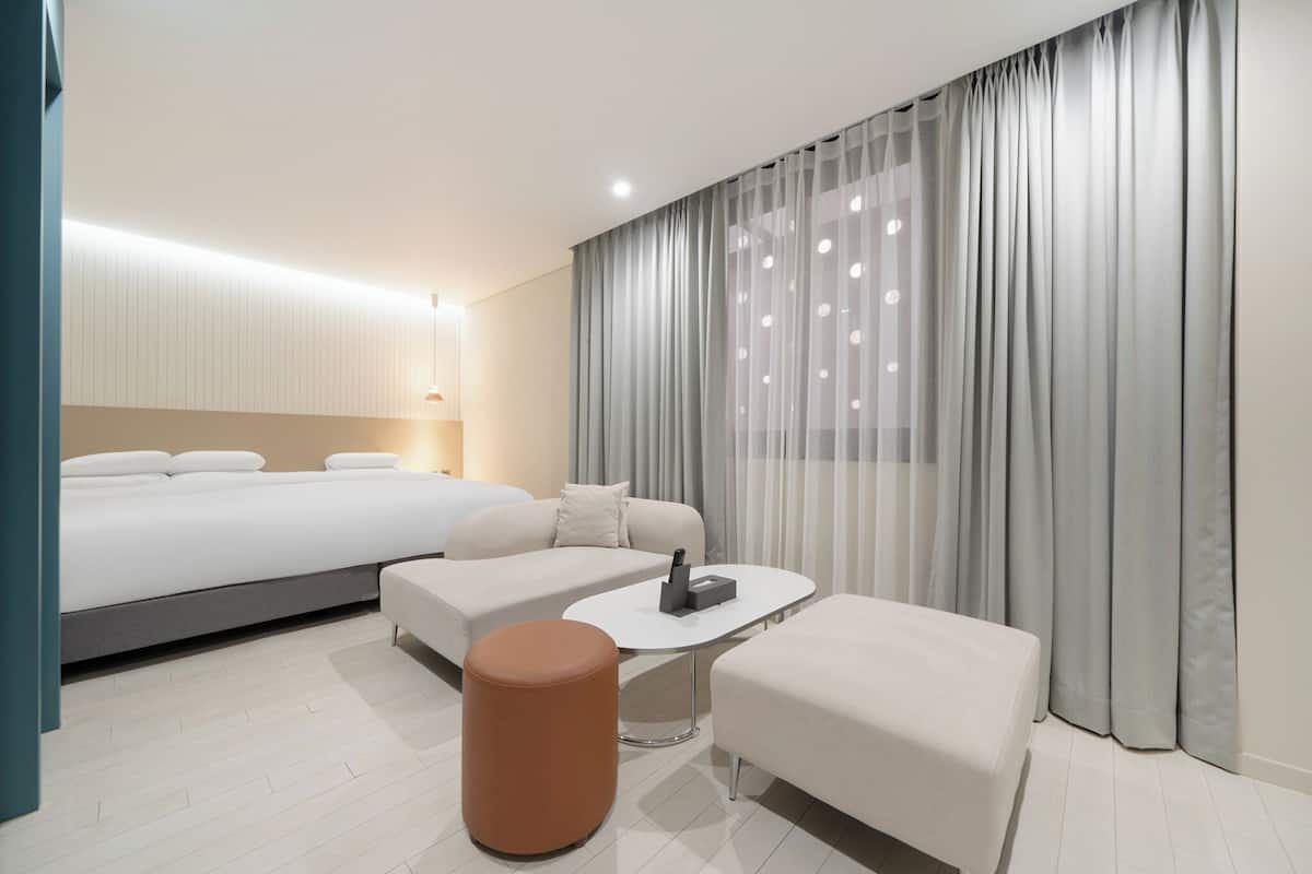 Ett modernt hotellrum med en stor säng, en soffa, ett soffbord och en liten pall.