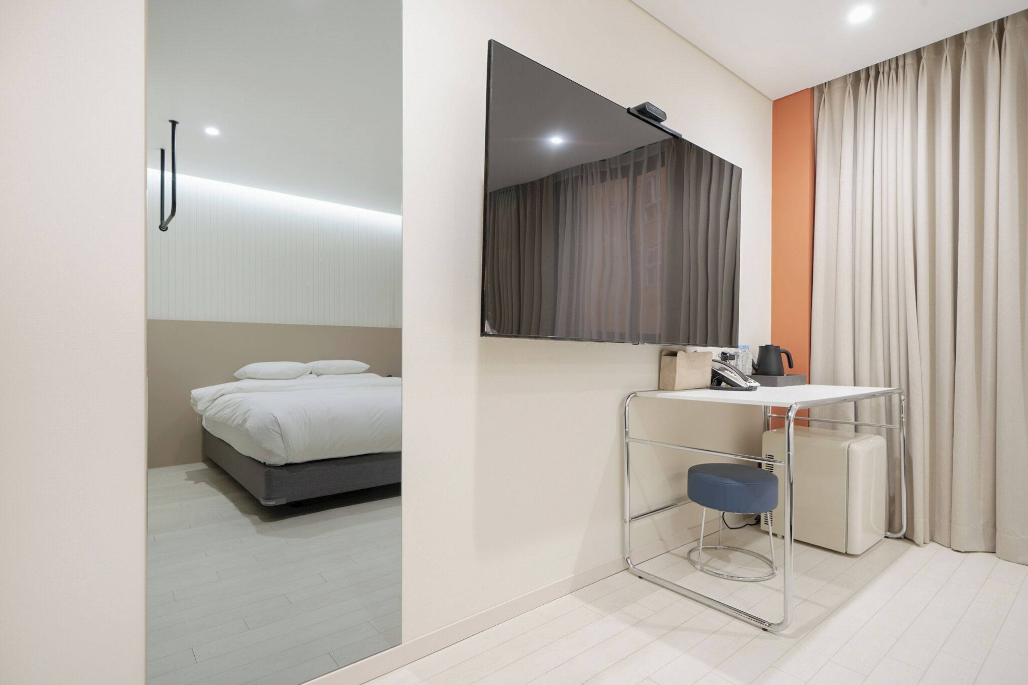 Quarto de hotel moderno com uma cama, uma escrivaninha com cadeira, um espelho e uma janela com cortinas.