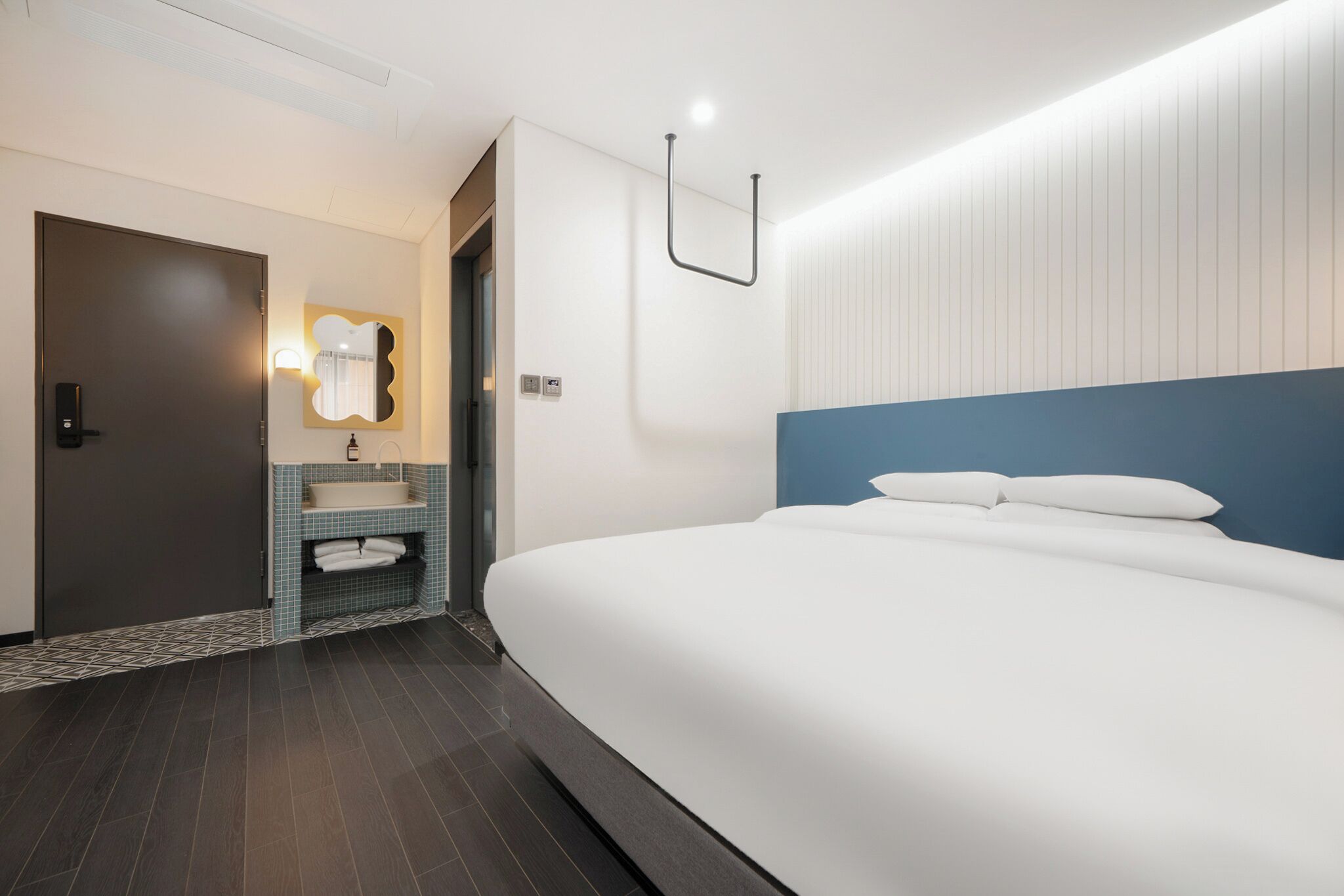 Una habitación de hotel moderna con una cama grande, un baño con lavamanos y espejo, y una puerta.