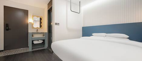 A modern hotel room with a large bed, a bathroom with a sink and mirror, and a door.