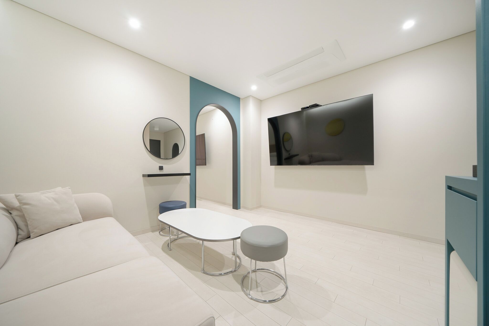 Ein modernes, minimalistisches Zimmer mit einem weißen Sofa, einem kleinen runden Tisch und einem grauen Hocker.