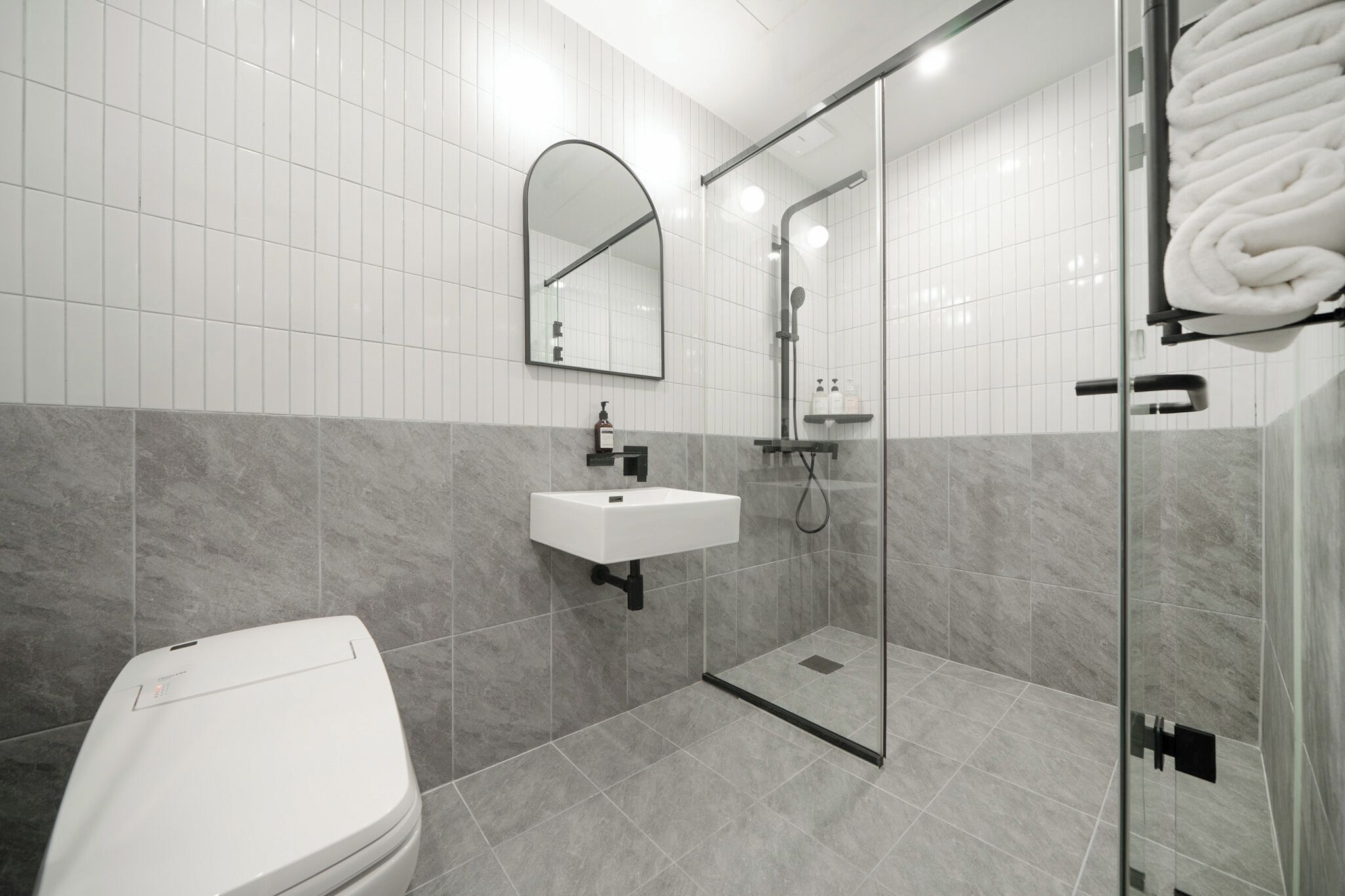 Un baño moderno con inodoro, lavamanos y cabina de ducha con mampara de vidrio.