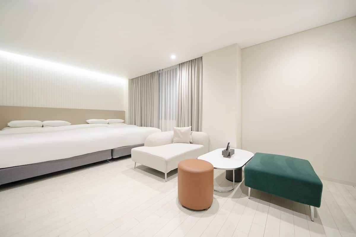Ett modernt hotellrum med en stor säng, en soffa, ett litet runt bord och en grön pall.