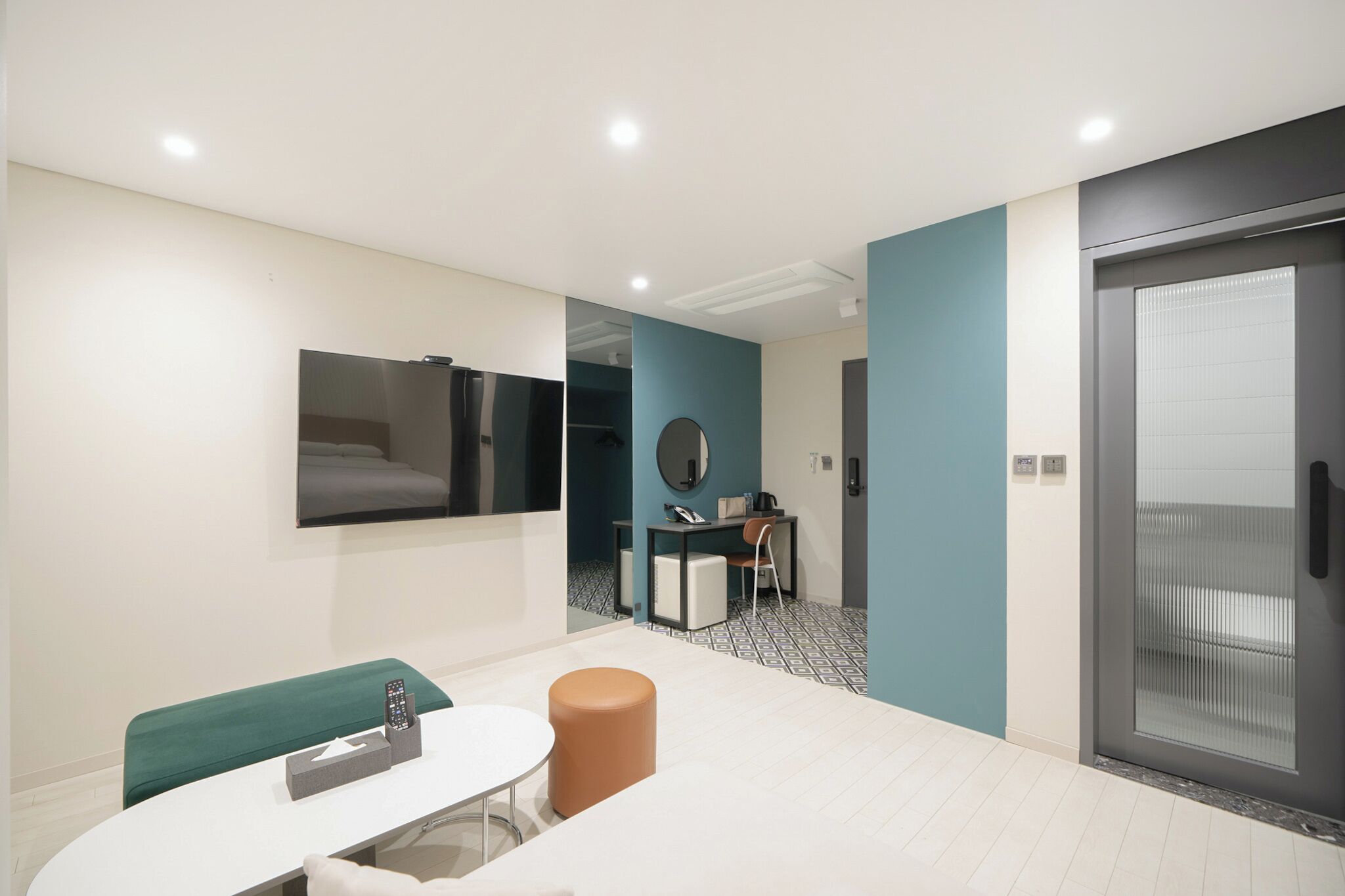 A modern hotel room with a bed, a desk, a chair, a mirror, and a door.