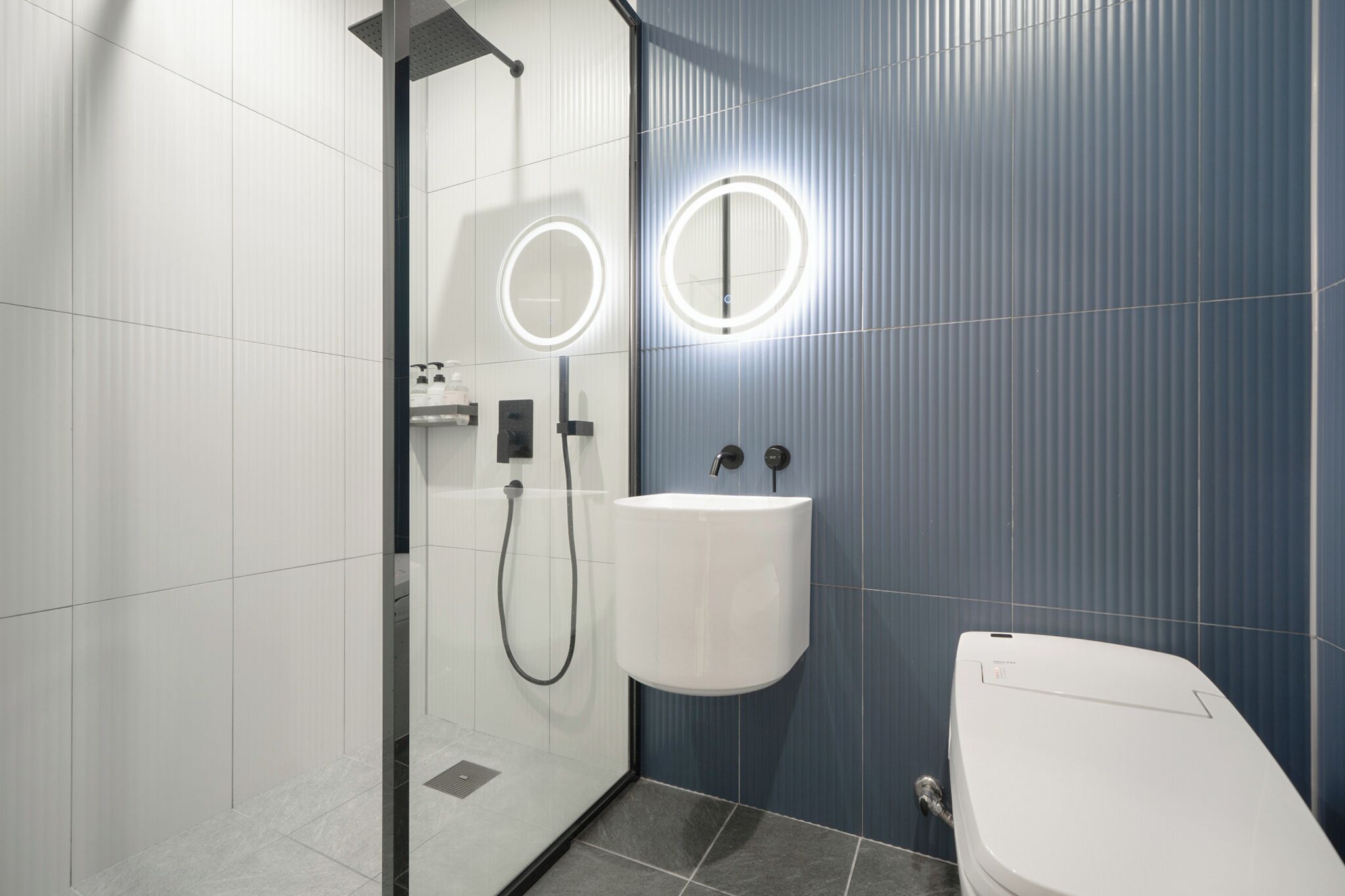 Un baño moderno con ducha de vidrio, lavamanos blanco y un inodoro.