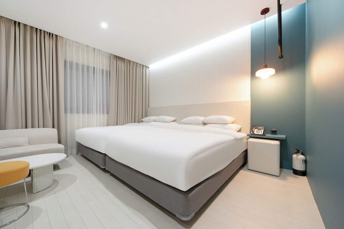 Ett modernt hotellrum med en stor säng, en soffa, ett litet bord och ett sängbord med en telefon och en flaska.