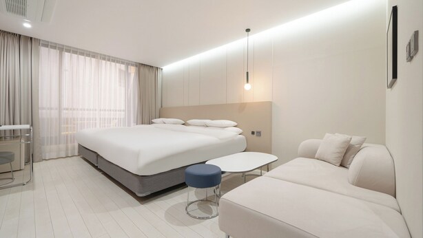 A modern hotel room with a large bed, a small table, a sofa, and a desk.
