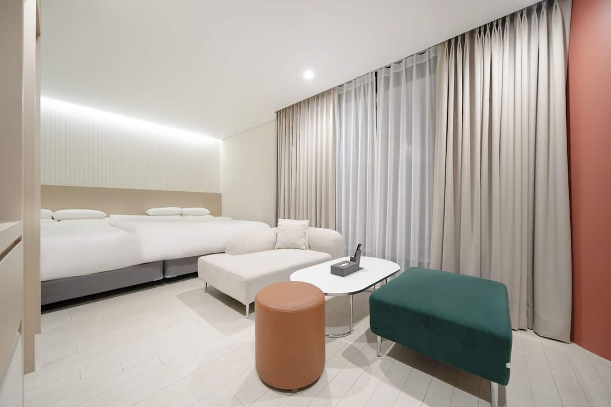 Ett modernt hotellrum med en stor säng, en soffa, ett litet bord och en grön pall.