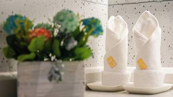 A bathroom with a white sink, two white towels with yellow text, and a potted plant with colorful flowers.