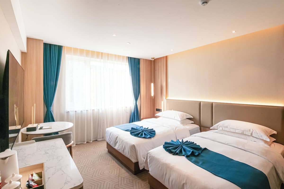 Habitación de hotel con dos camas, una mesa redonda, un televisor y una ventana con cortinas.