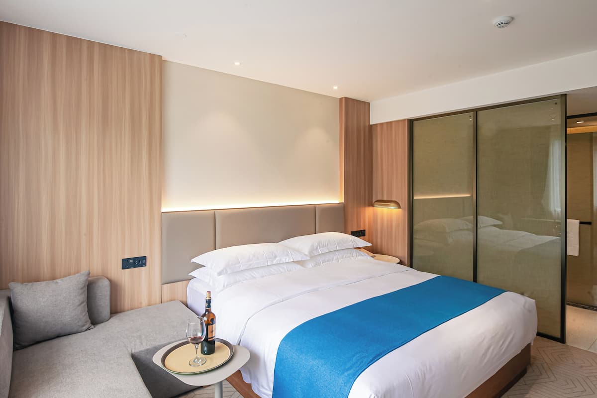Una habitación de hotel moderna con una cama grande, una zona de estar con una pequeña mesa y un separador de vidrio.