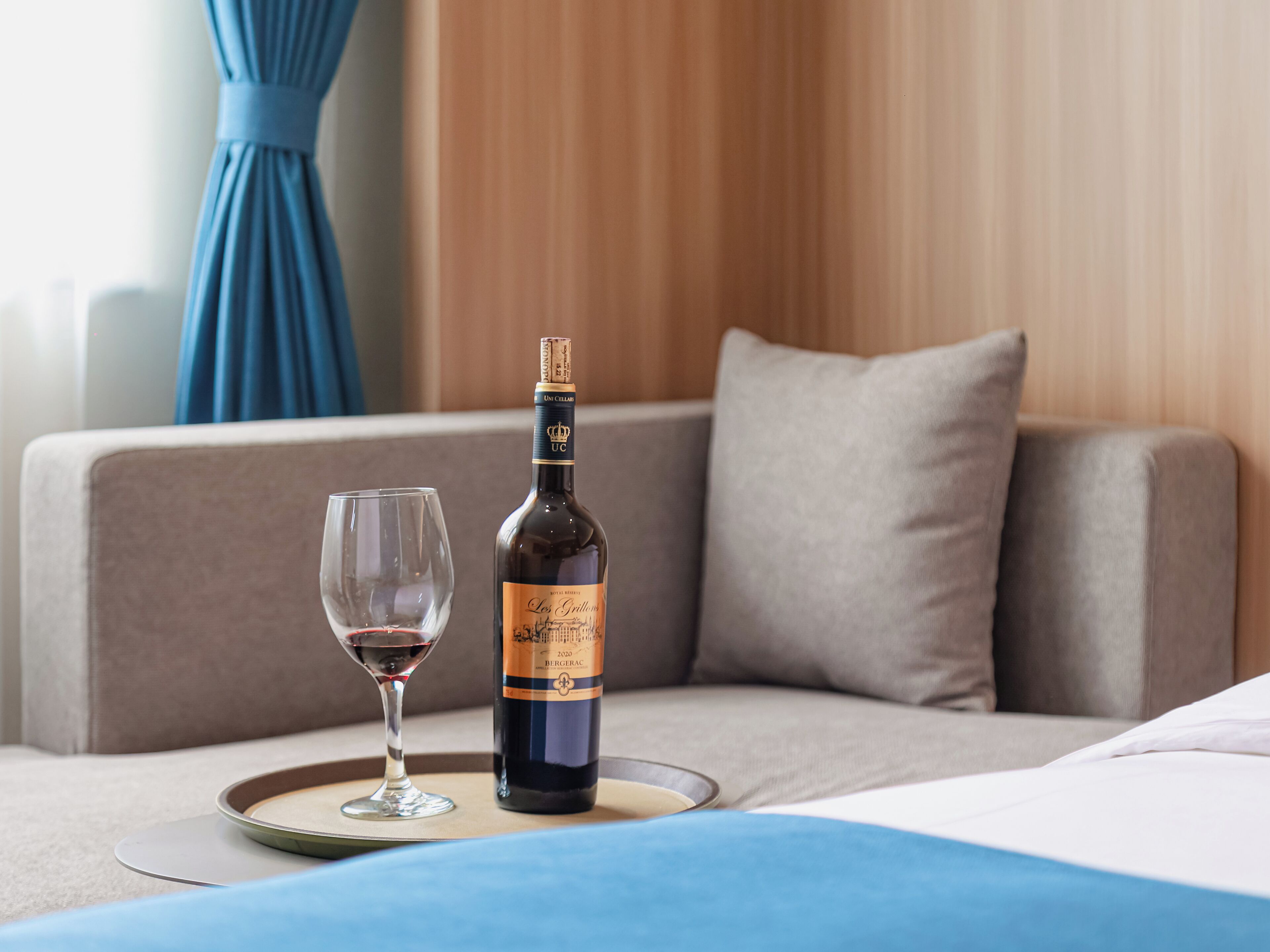 A bottle of wine and a glass on a tray on a bed.