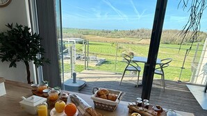 A breakfast table with various food items and a view of a green landscape through large windows. - Rèverie en Périgord du Domaine des Hauts de Rouquette (Eymet)