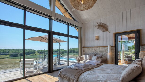 A bedroom with a large window, a bed, a stone wall, and a view of a pool and landscape. - Rèverie en Périgord du Domaine des Hauts de Rouquette (Eymet)