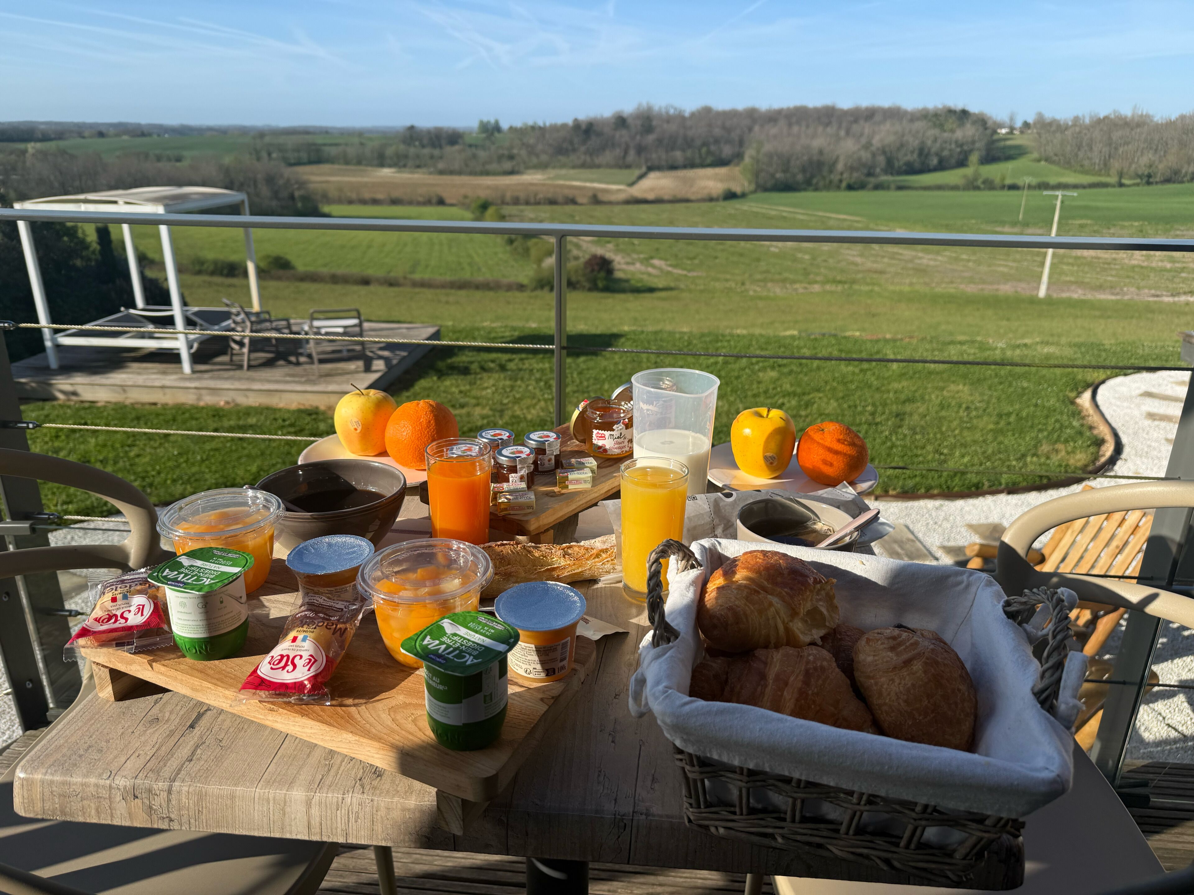 A breakfast table with food and drinks on a balcony overlooking a rural landscape.