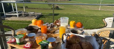 A breakfast table with food and drinks on a balcony overlooking a rural landscape.