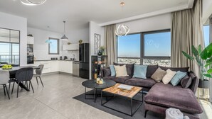 A modern living room with a dark-colored sofa, a coffee table, and a dining area with a white table and chairs.