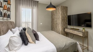 A modern bedroom with a bed, a desk, a TV, and a wall-mounted light fixture.