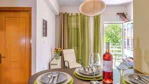 A dining area with a wooden table set for four, a bottle of red wine, and a vase with flowers. - Alisahni Home 1, Villa (Chania)