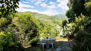 A stone pathway leading to a table set for dining, surrounded by lush greenery and a view of a hillside with buildings. - Nonna Lena by Interhome (Molini di Prelà)